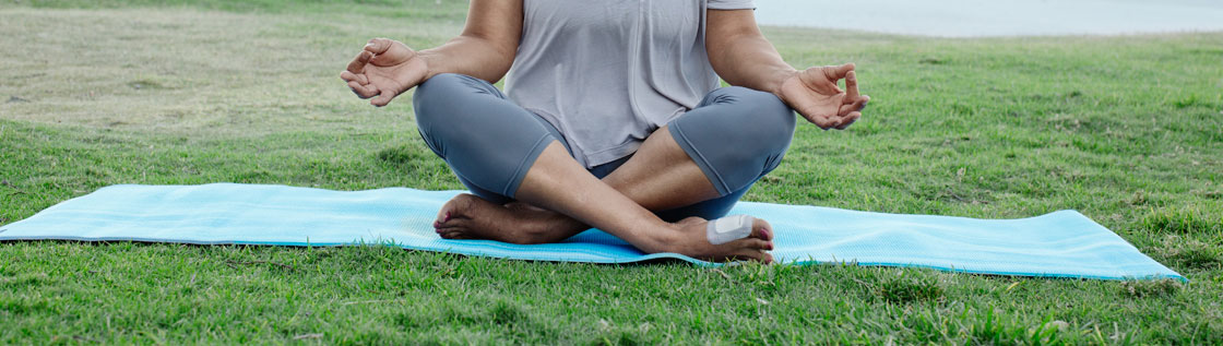 Kvinde sidder i yoga position, har sårbandage på foden